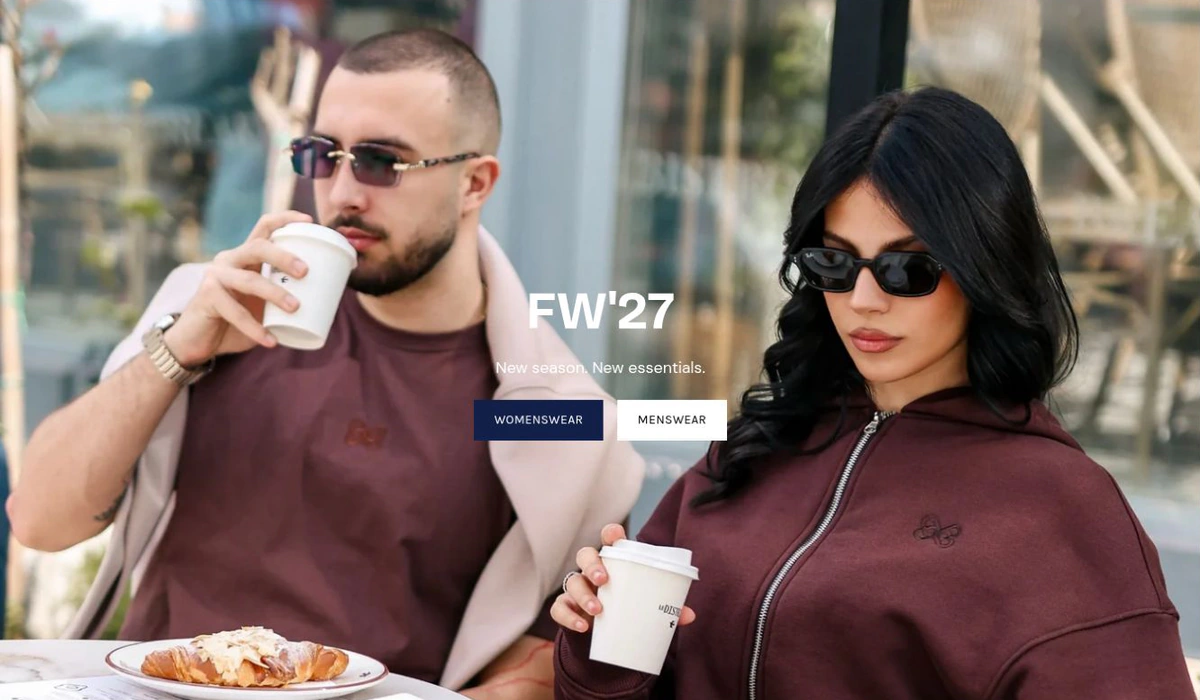 Two people in burgundy clothing outside a café in the saved FW’27 campaign.