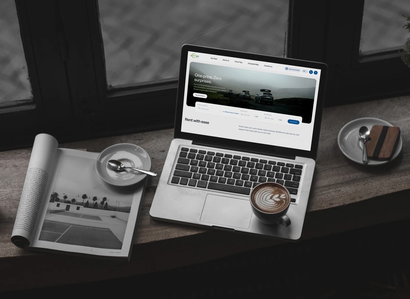 Green Light Car Rental website on a MacBook at a café counter with coffee and a magazine.
