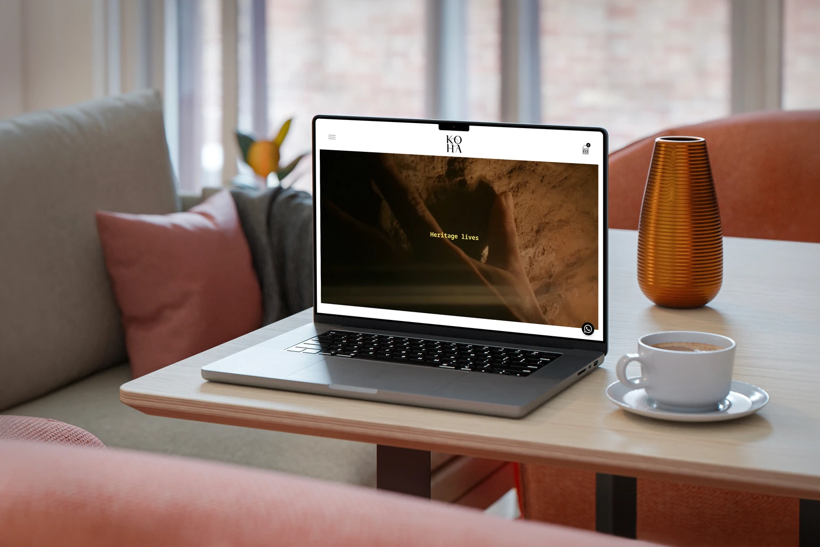 Koha Eyewear website displayed on a MacBook on a cafe table beside a coffee cup and amber vase.