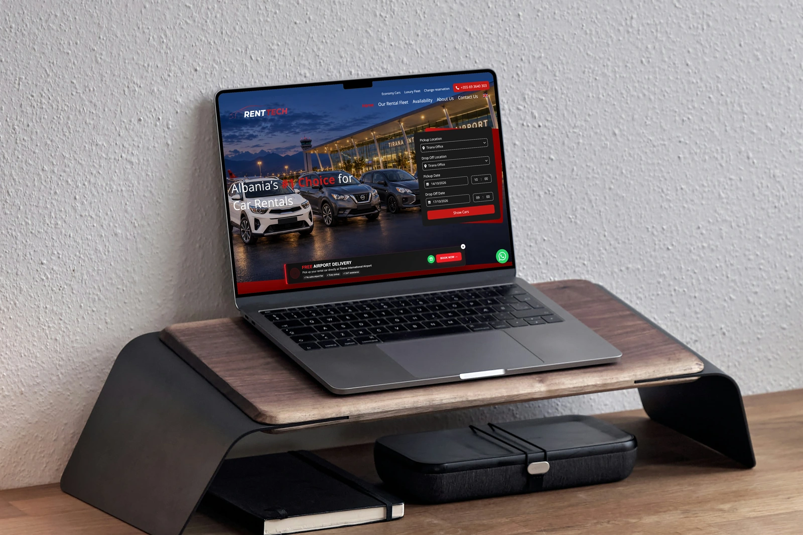 RentTech car-rental booking website on a MacBook on a wooden workstation stand.